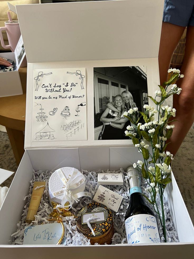 Bridesmaid proposal box with a black and white photo of bride and bridesmaid, bottle of wine with a personalized label, a candle and a mix-match of beauty products.