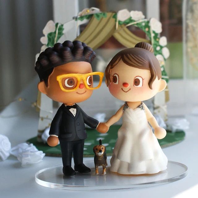 A cake topper depicting a bride and groom as characters from Animal Crossing. A dog figurine is also shown between them.