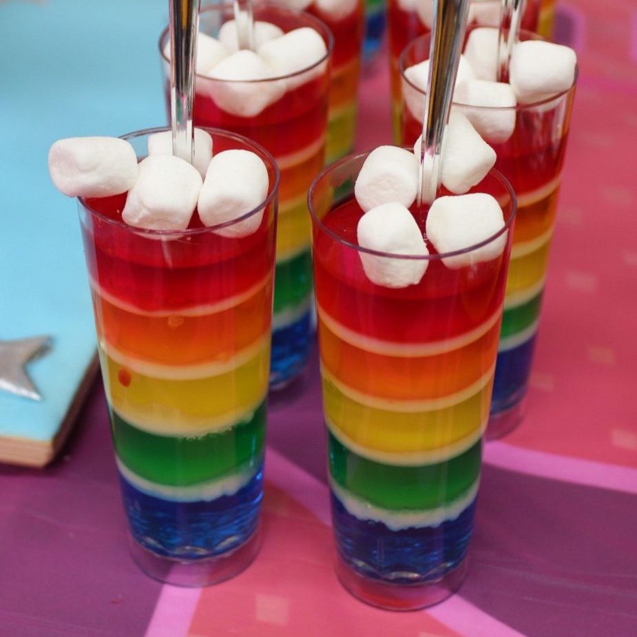 Rainbow striped parfait-style jello desserts topped with white marshmallows. 