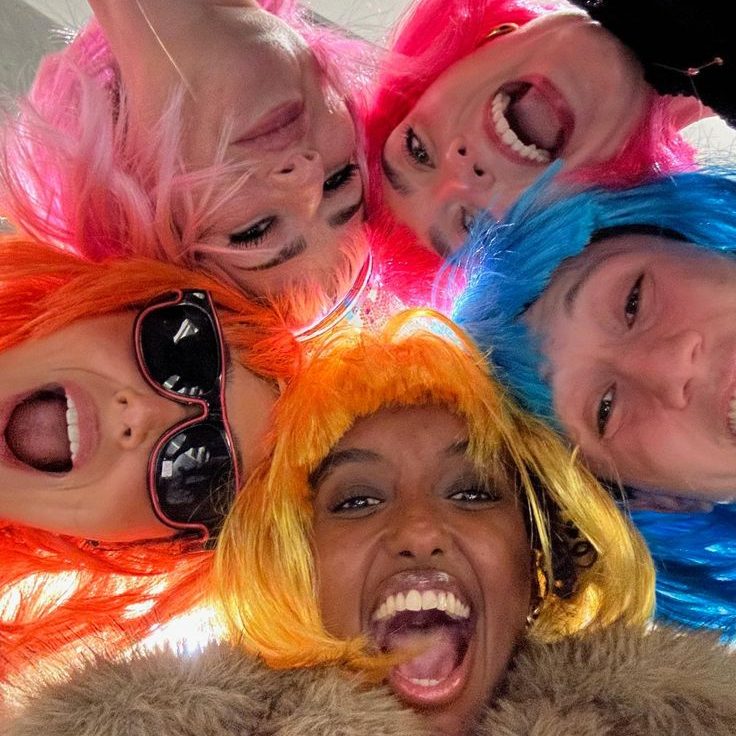 Five friends wearing different brightly colored wigs smiling for a photo together.