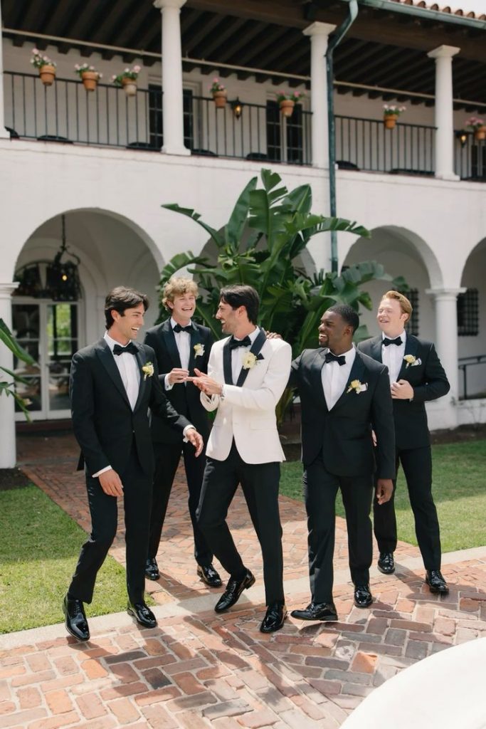 A picture of a happy groom and four groomsmen in black tie formal attire.