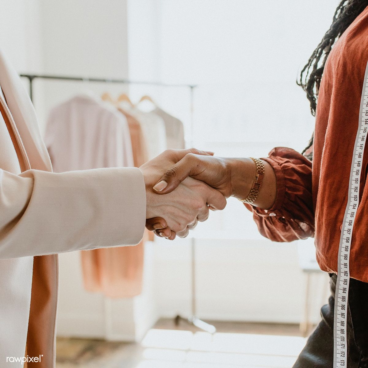A wedding planner shakes hands with a clothes designer inside the designer's studio.