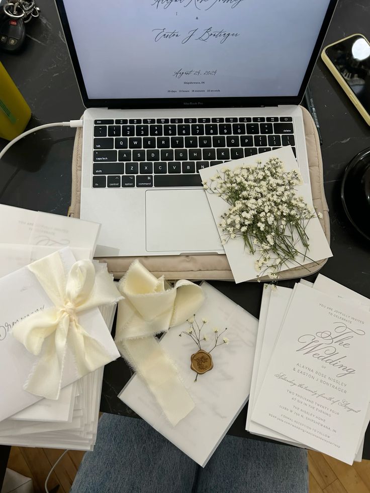 A wedding planner's workspace, filled with samples of invitations, baby's breath flowers, wax stamps, and a laptop to keep track of all the details.