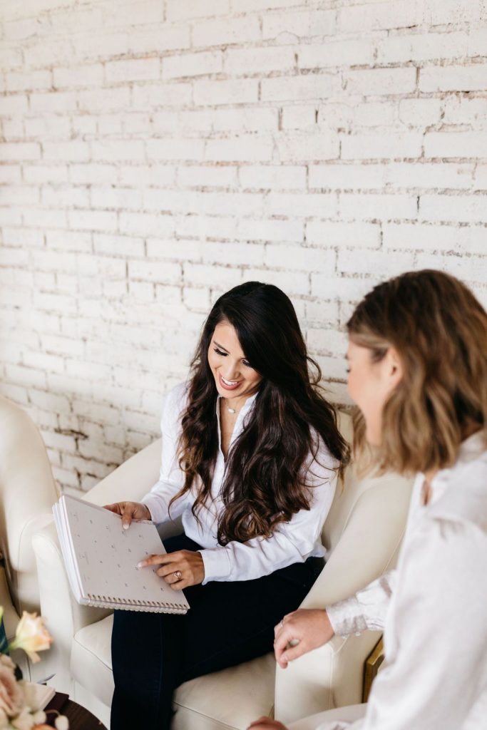 A wedding planner chats with their engaged client about the timeline and little details of the wedding as they both look at a calendar.