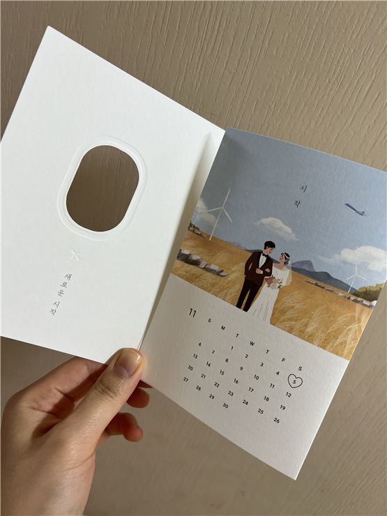 A wedding invitation with a calendar design is held up against a cream-colored wall.