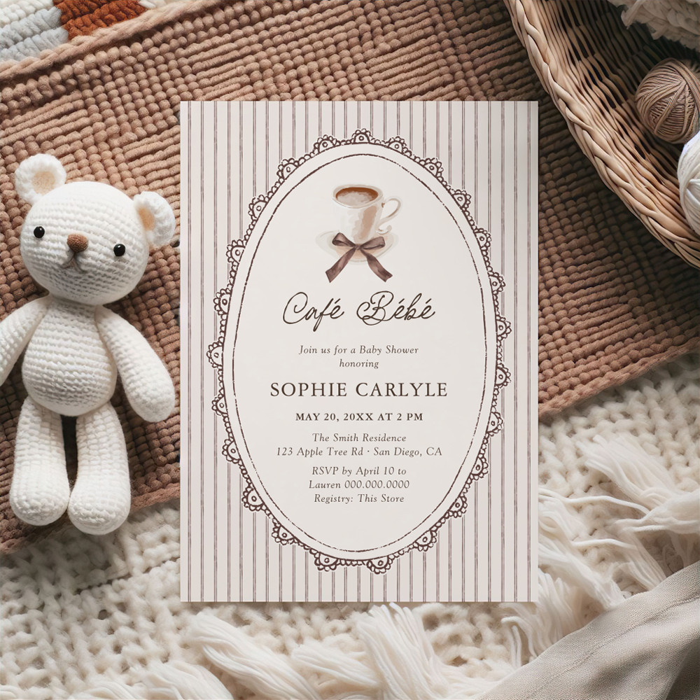 A Café Bébé baby shower invitation on beige striped background with vintage lace oval frame, featuring coffee cup with brown ribbon bow and elegant script typography, displayed with crocheted teddy bear on textured rug.