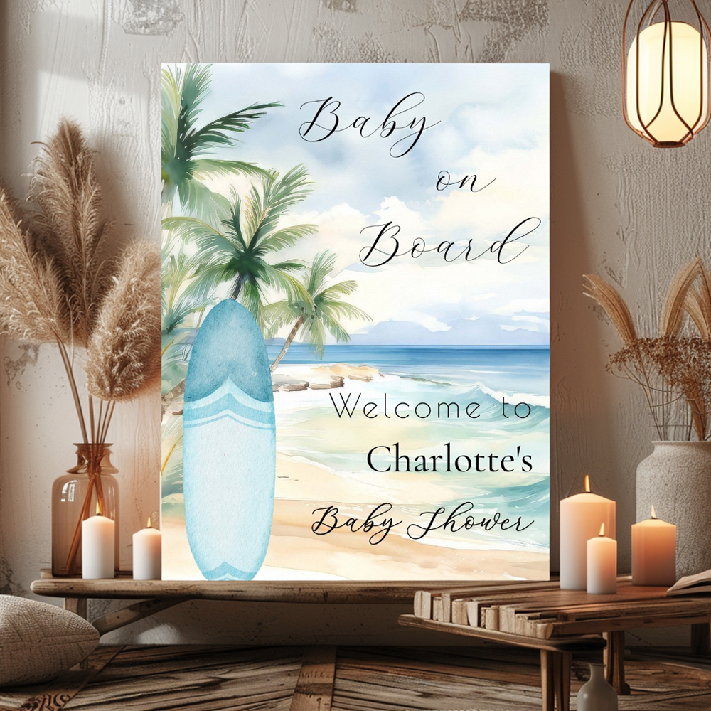 A Baby on Board beach-themed baby shower sign featuring watercolor tropical beach scene with palm tree, surfboard, ocean waves, and sand, displayed with pampas grass and candles on wooden shelf.