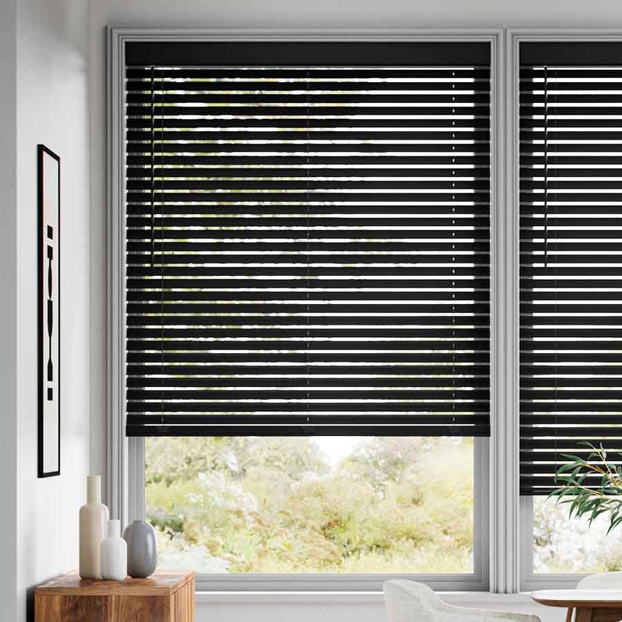 Black venetian blinds shown on a window. In the background there is a wooden table with a few vases. 