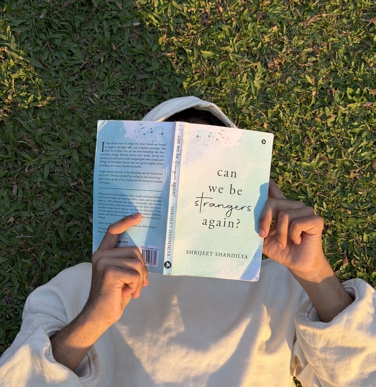 A man is lying on the grass outside, reading a book.