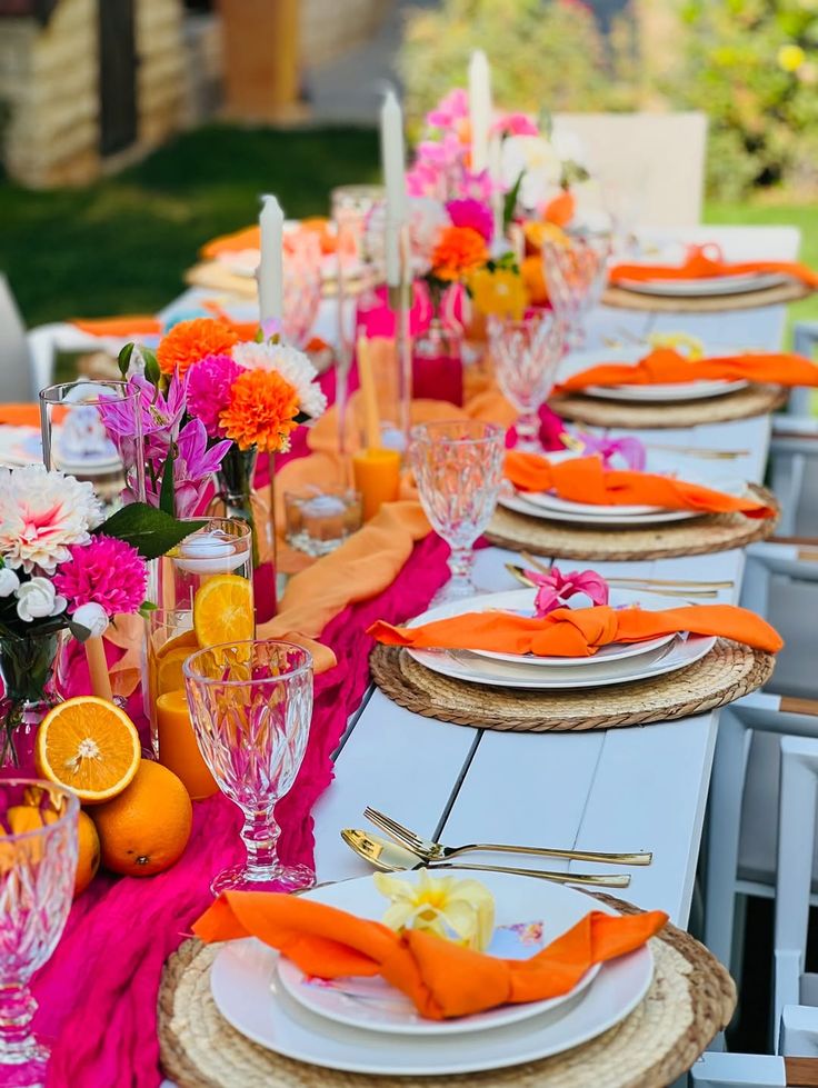 A colorful table display with glasses, napkins, and plates. Fruit and flowers are also being used to decorate the table. 