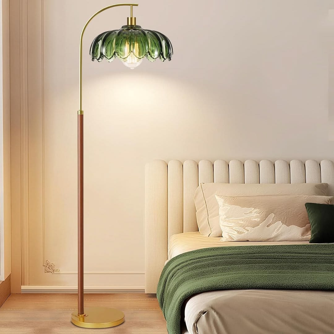 A green glass floor lamp is shown lighting next to a cream bed with a green throw blanket and green pillow.