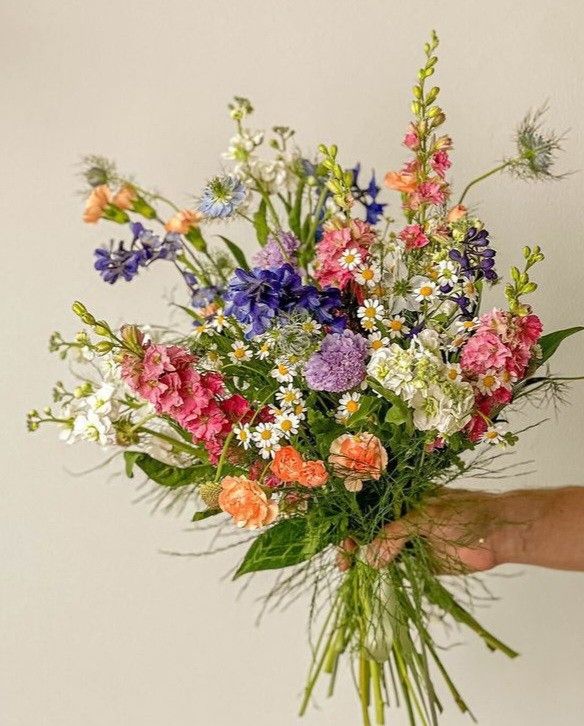 A large bouquet of fresh flowers in shades of blue, pink, white and orange with strands of greenery at the bottom.