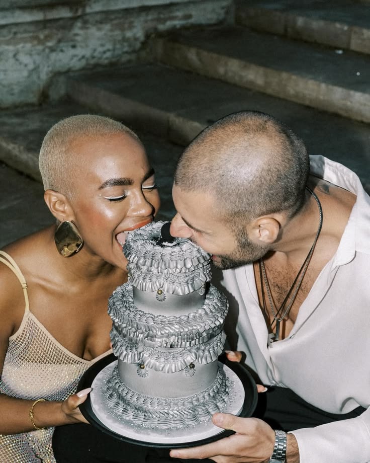 A couple biting a silver metalic three-tier wedding cake.