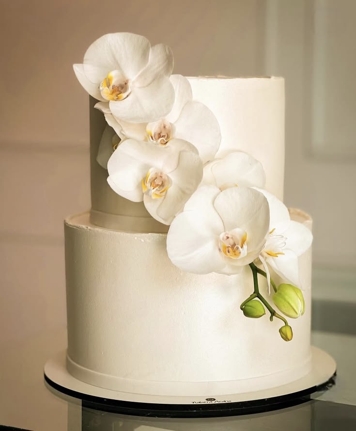 A simple white two-tier wedding cake decorated with white orchid flowers.